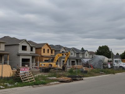 A row of partially built homes in Brockville, Ontario, with abandoned plans and construction gear in the foreground, symbolizing a failed joint venture and ensuing legal dispute.
